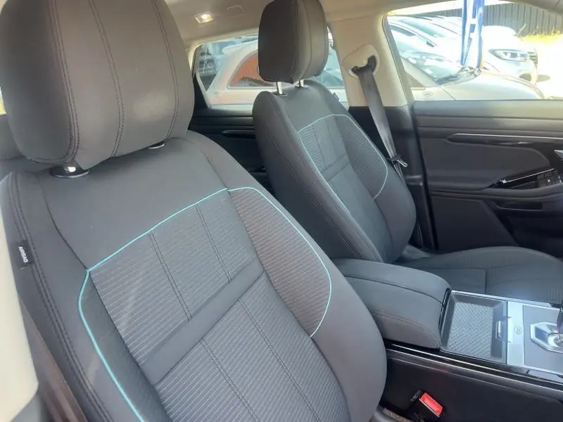 Vue intérieure montrant les sièges avant noirs avec surpiqûres bleues et console centrale du Range Rover Evoque Indus Silver 2019.