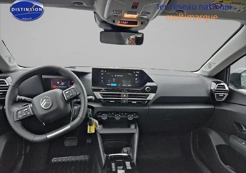 Vue avant intérieure du poste de conduite d'une Citroën C4 gris mercury, avec écran tactile central et volant cuir noir.