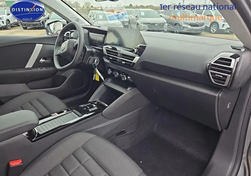 Intérieur avant droit de la Citroën C4 1.2 hybride 136 plus 2025, avec tableau de bord moderne et sièges tissu noir.