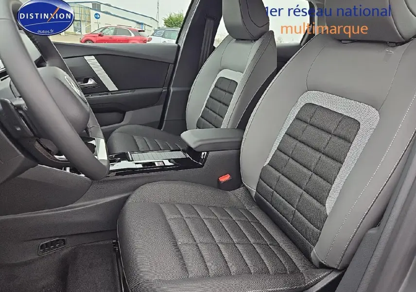Intérieur de la Citroën C4 hybride 2025, vue côté conducteur sur sièges tissu noir et gris avec accoudoir central.