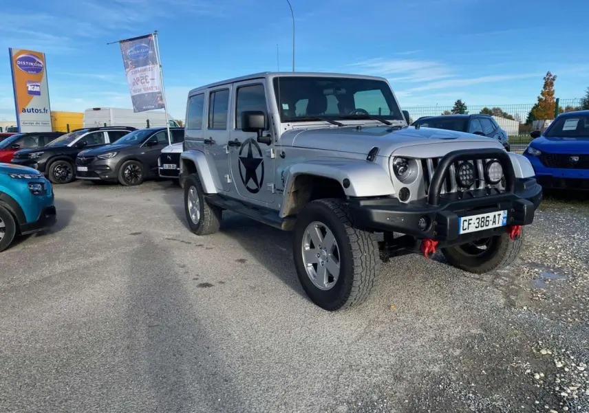 Jeep Wrangler gris clair vue 3/4 avant droit avec étoile noire sur porte et pare-buffle équipé de phares additionnels.