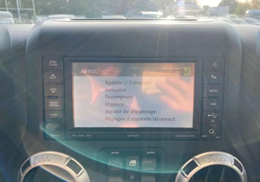 Écran central tactile du système Uconnect sur Jeep Wrangler gris clair 2012, avec commandes autour et reflets lumineux.