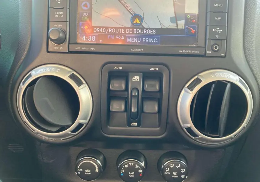 Vue rapprochée du tableau de bord du Jeep Wrangler gris clair 2012, montrant les aérateurs ronds et la console centrale avec commandes.