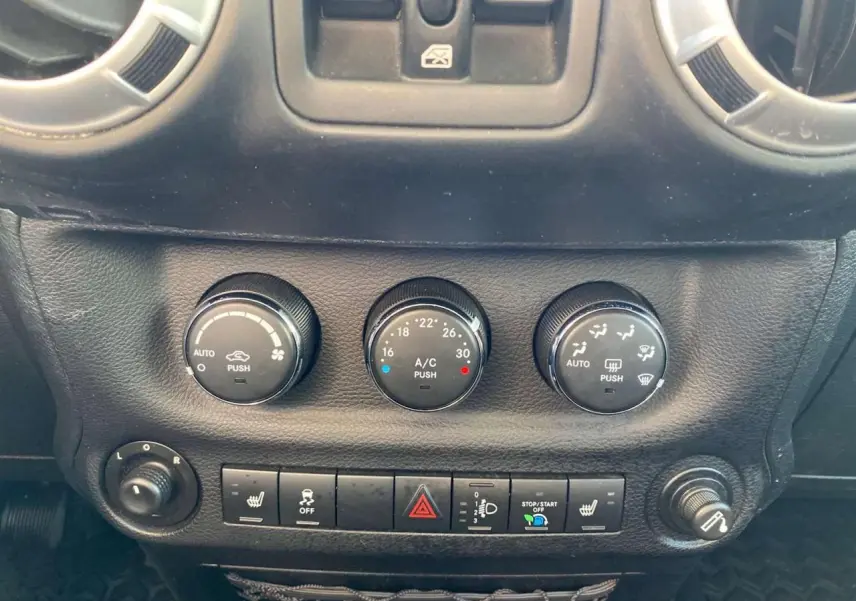 Gros plan sur les commandes de climatisation et les boutons de fonction du tableau de bord du Jeep Wrangler gris clair 2012.