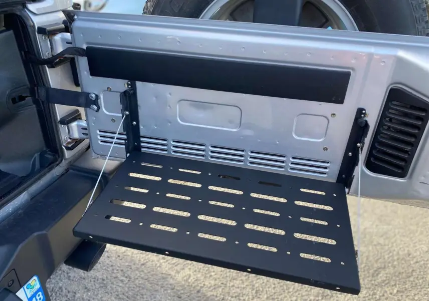 Vue rapprochée de la porte arrière ouverte gris clair du Jeep Wrangler 2012 avec tablette rabattable noire intégrée.