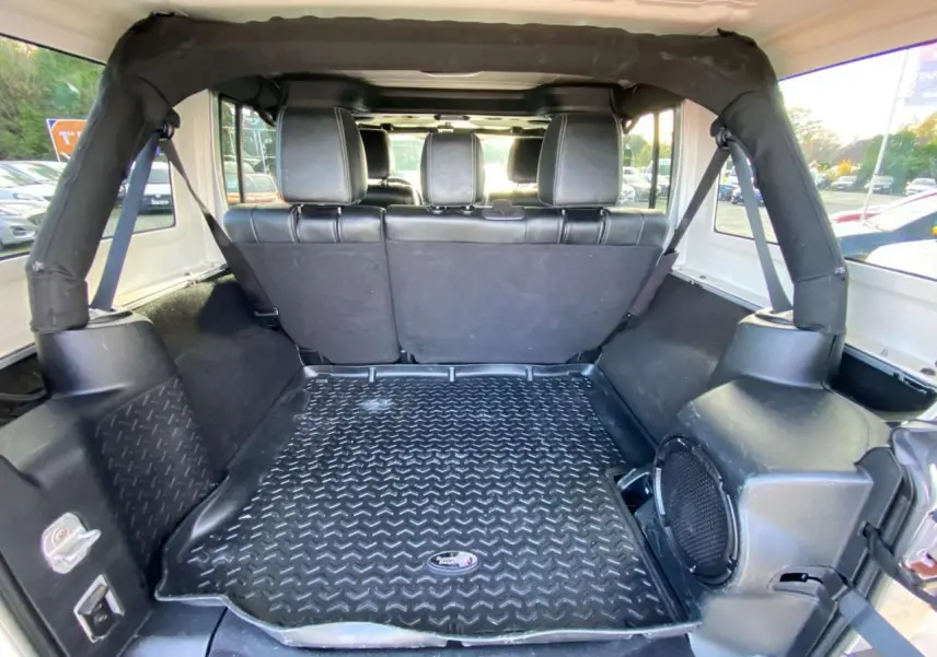 Vue intérieure arrière du coffre d'un Jeep Wrangler gris clair 2012 avec banquette et tapis de sol caoutchouc.