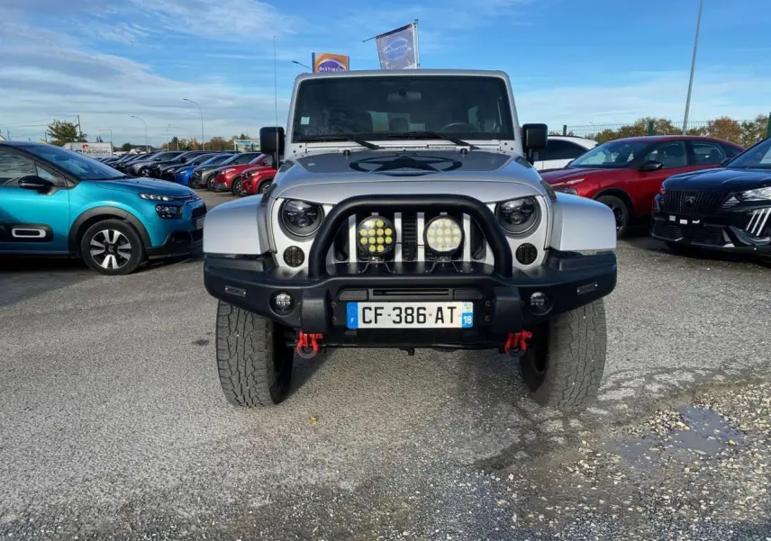 Vue de face d'un Jeep Wrangler gris clair 2012 avec pare-buffle noir et phares additionnels ronds.