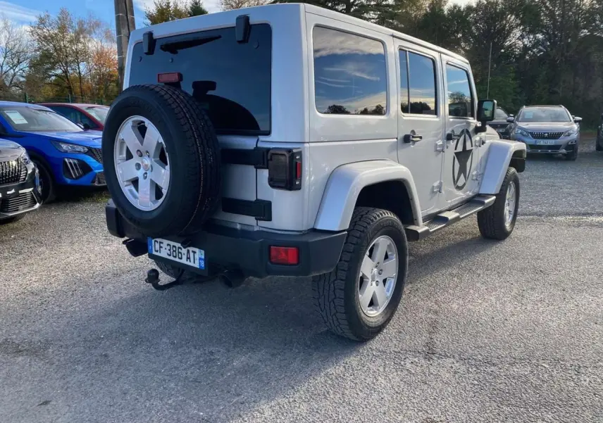Jeep Wrangler 2.8 CRD 200 Unlimited gris clair vue 3/4 arrière droit avec roue de secours et étoile noire sur porte.