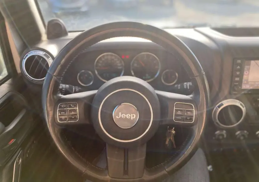 Vue intérieure centrée sur le volant Jeep du Wrangler 2012, avec tableau de bord et commandes visibles en arrière-plan.