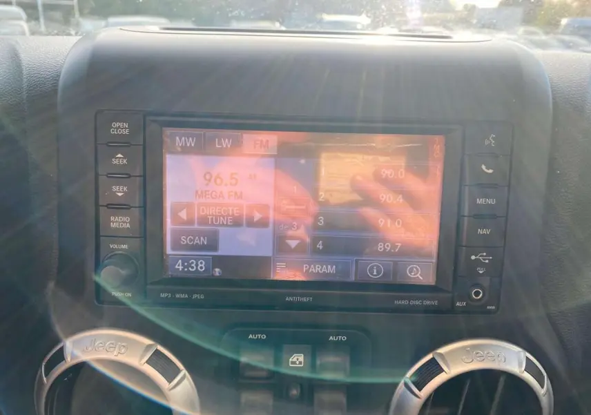 Écran multimédia allumé au centre du tableau de bord d'un Jeep Wrangler gris clair de 2012, avec commandes autour.