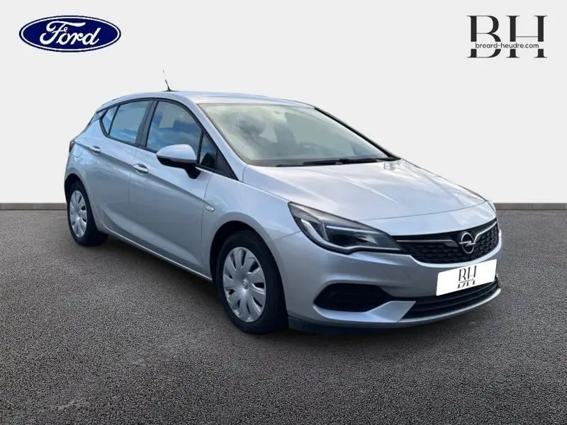 Vue 3/4 avant d'une Opel Astra gris minéral, avec calandre noire et jantes à enjoliveurs, sur fond neutre.