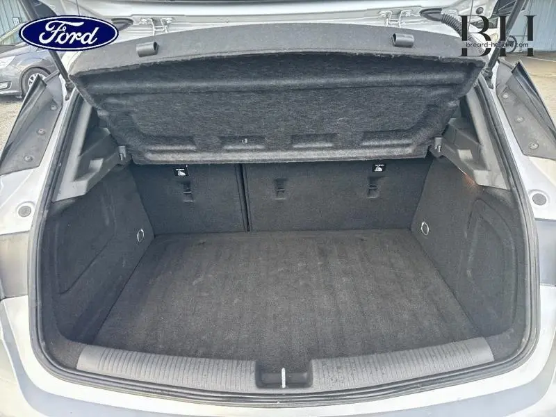 Coffre ouvert d'une Opel Astra gris minéral, vue de l'arrière montrant l'espace de chargement vide et la banquette rabattable.