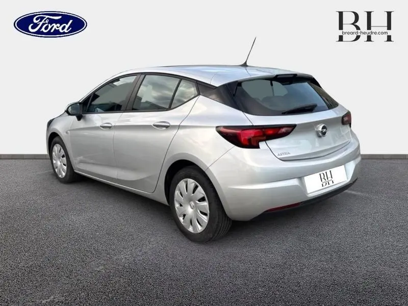 Vue 3/4 arrière droite d'une Opel Astra gris minéral avec feux arrière foncés et jantes tôles avec enjoliveurs.