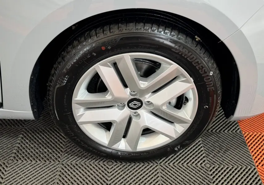 Gros plan sur la roue avant droite d’une Renault Clio gris clair, mettant en valeur la jante aluminium au design moderne.