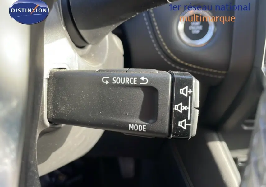 Gros plan sur la commande au volant avec boutons source et mode, intérieur cuir noir visible en arrière-plan.