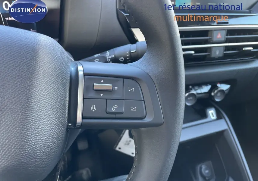 Gros plan sur les commandes au volant à gauche d'une Citroën C4 Hybrid 2026, intérieur noir avec tableau de bord moderne.