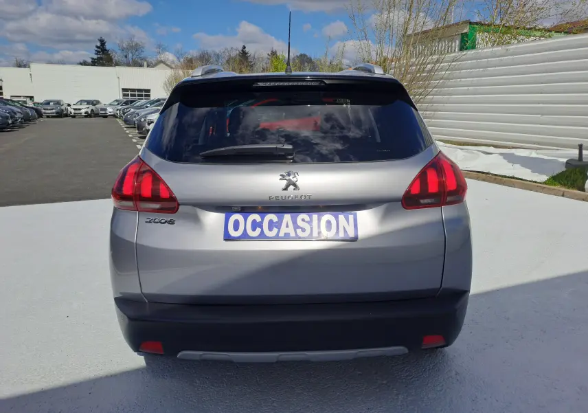 Vue arrière d'un Peugeot 2008 gris avec feux rouges et plaque "OCCASION" en extérieur sous un ciel partiellement nuageux.
