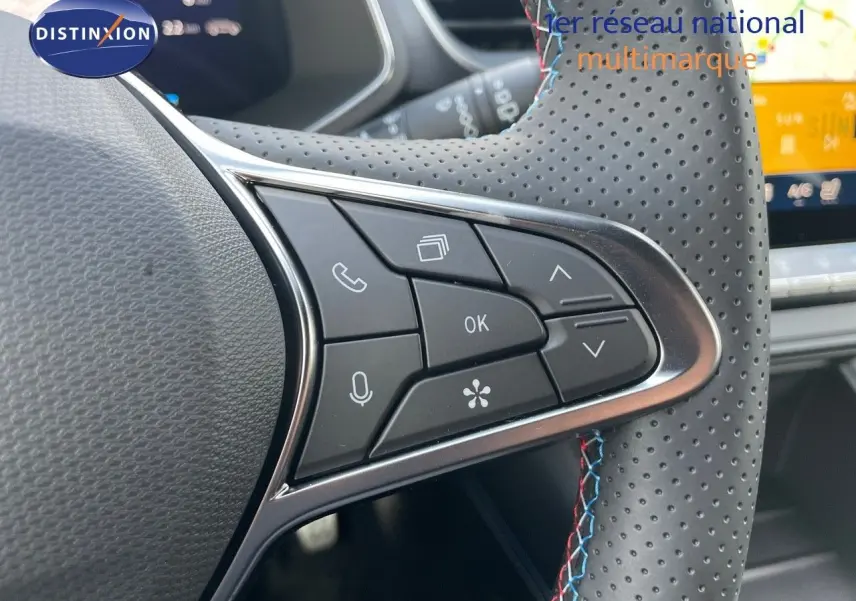 Gros plan sur les commandes du volant perforé avec surpiqûres tricolores du Renault Symbioz gris Rafale 2024.