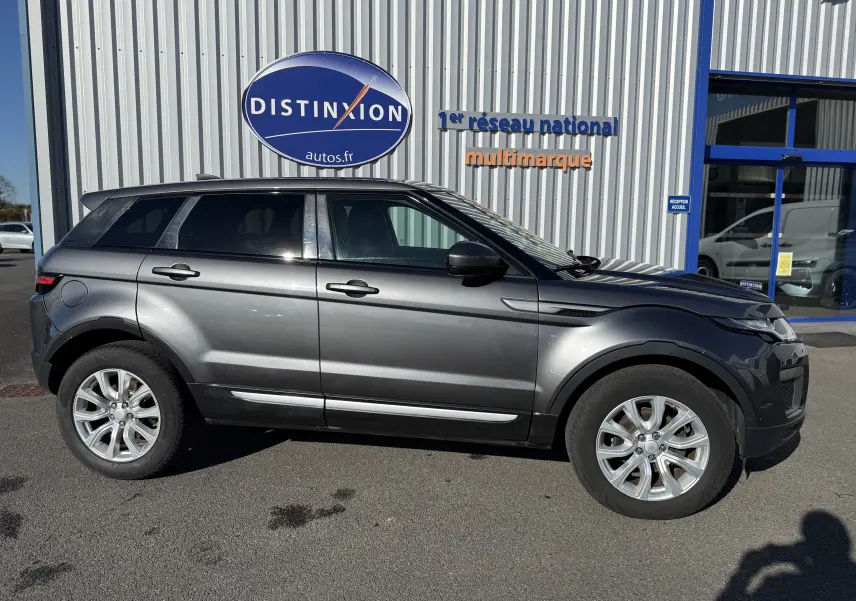 Vue de profil côté gauche d'un Range Rover Evoque gris métallisé garé devant un bâtiment avec enseigne Distinxion.