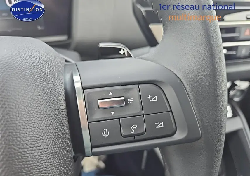 Gros plan sur les commandes audio et vocales au volant cuir de la Citroën C4 blanche Okenite 2025.