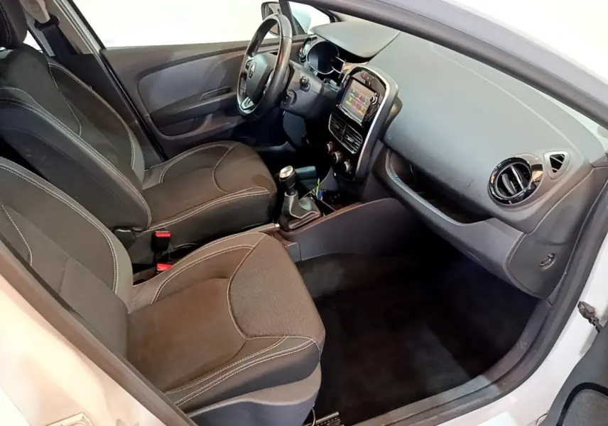 Vue intérieure côté conducteur de la Renault Clio blanche 2016, montrant sièges noirs et tableau de bord avec écran tactile.