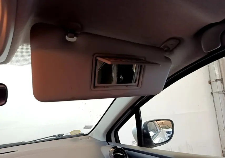 Détail intérieur montrant le pare-soleil côté conducteur avec miroir et rétroviseur extérieur d’une Renault Clio blanche.