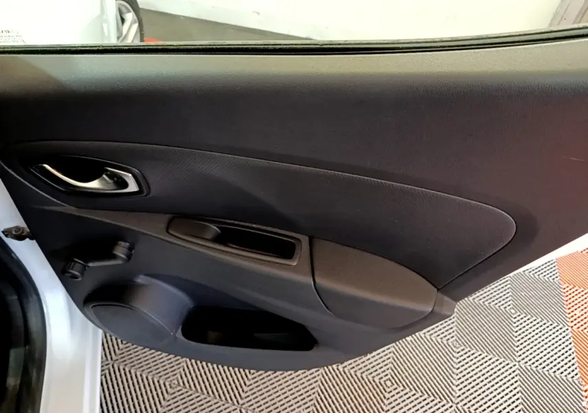 Vue intérieure de la porte côté gauche d'une Renault Clio Zen Energy dCi 75 blanche, avec poignée chrome et manivelle de vitre.