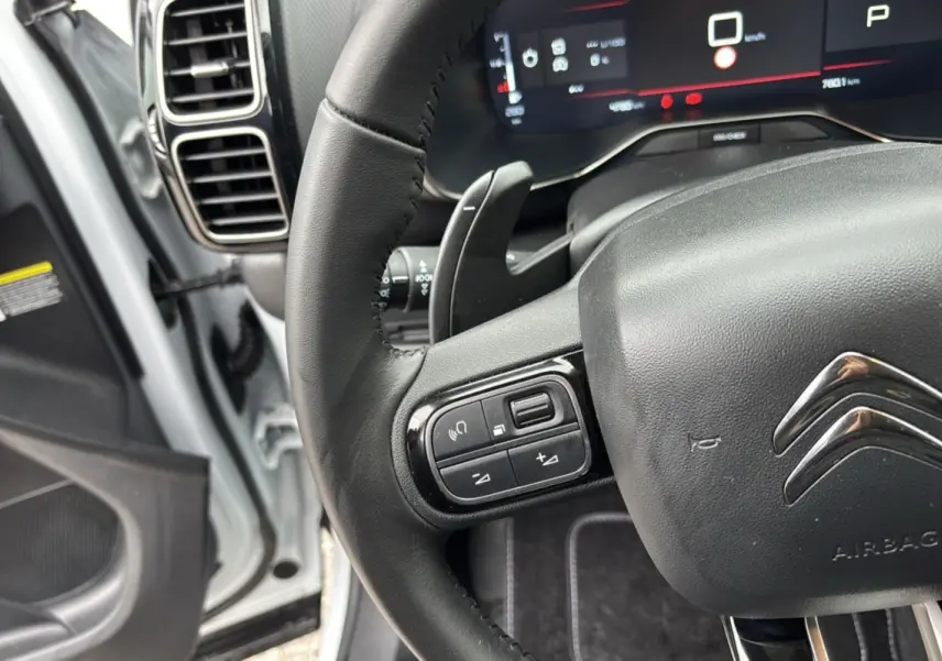 Gros plan sur le volant cuir multifonctions de la Citroën C5 Aircross Hybrid blanche, avec tableau de bord digital en arrière-plan.