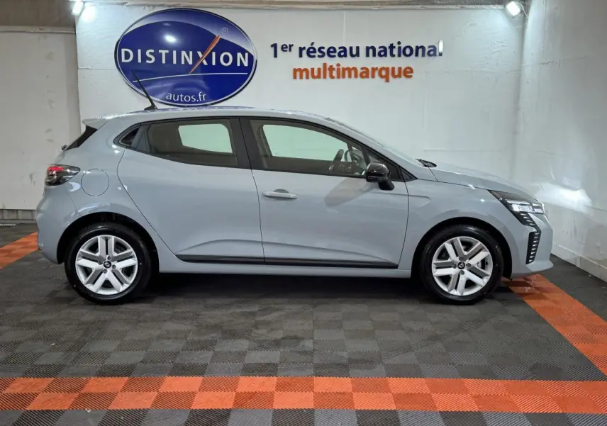 Profil côté droit de la Renault Clio gris clair 2025 avec feux LED et jantes alliage dans un showroom.