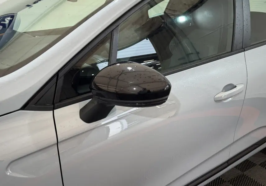 Rétroviseur noir brillant côté gauche d'une Renault Clio gris clair vue de profil avant en intérieur.