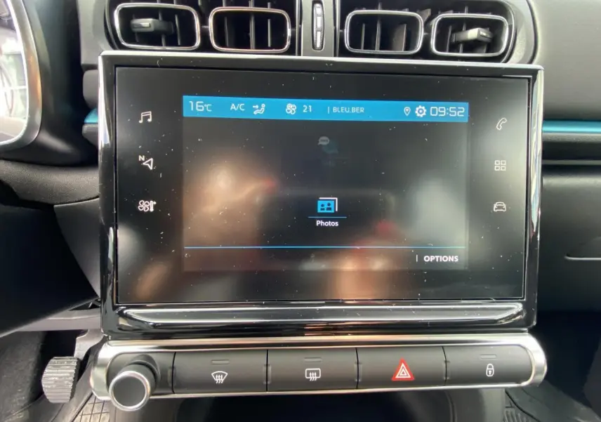 Écran tactile central et commandes de climatisation dans l'habitacle noir de la Citroën C3 Shine 2021.