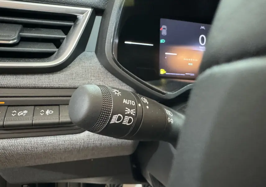 Gros plan sur la commande des feux à gauche du volant dans l’habitacle gris clair de la Renault Clio Evolution 2025.