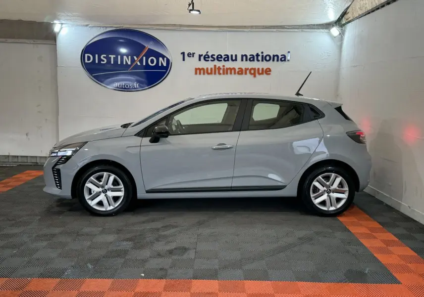 Profil droit d'une Renault Clio gris clair 2025 garée en intérieur avec feux LED et jantes alliage visibles.