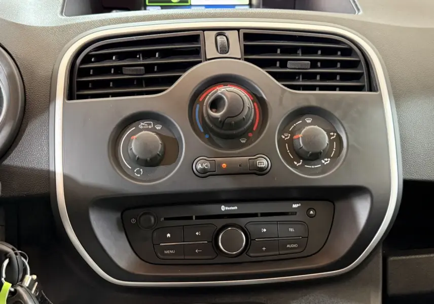 Vue rapprochée du tableau de bord noir du Renault Kangoo blanc 2021, montrant les commandes de climatisation et audio.