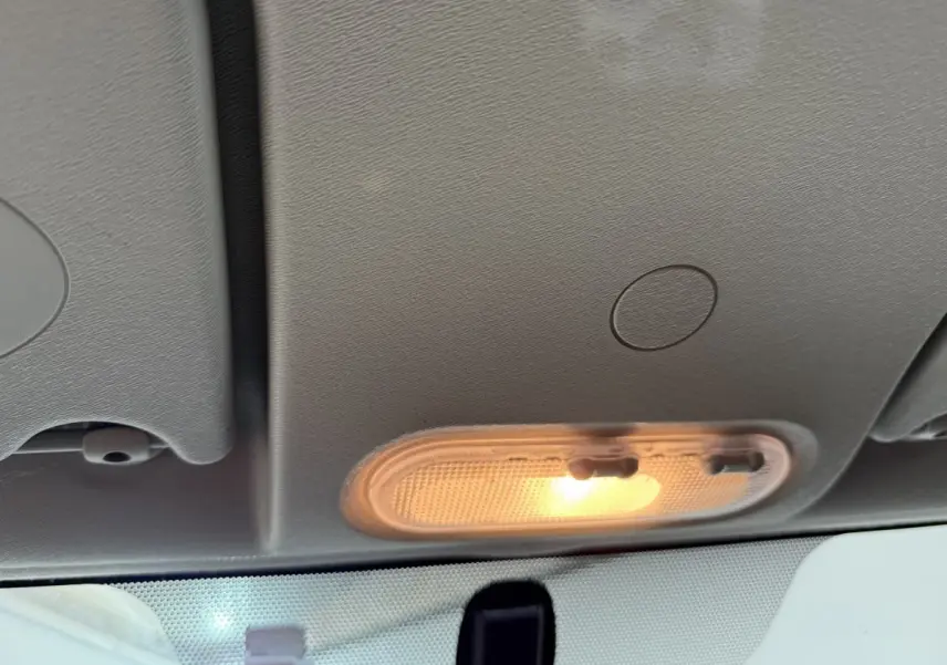 Plafonnier avant allumé vu de l'intérieur d'un Renault Kangoo blanc, avec toit clair et pare-brise partiel visible.