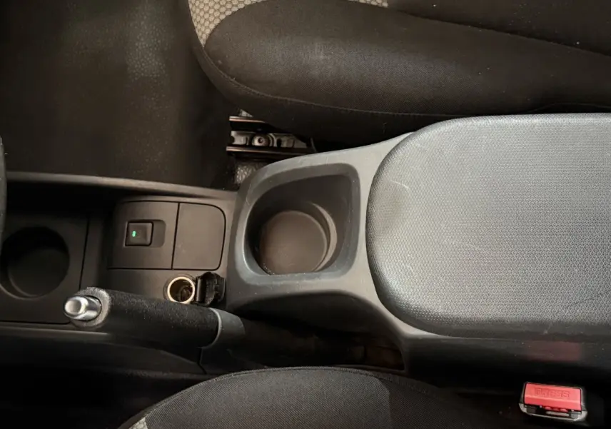 Vue intérieure centrée sur la console centrale noire avec frein à main et accoudoir entre sièges tissu gris et noir.