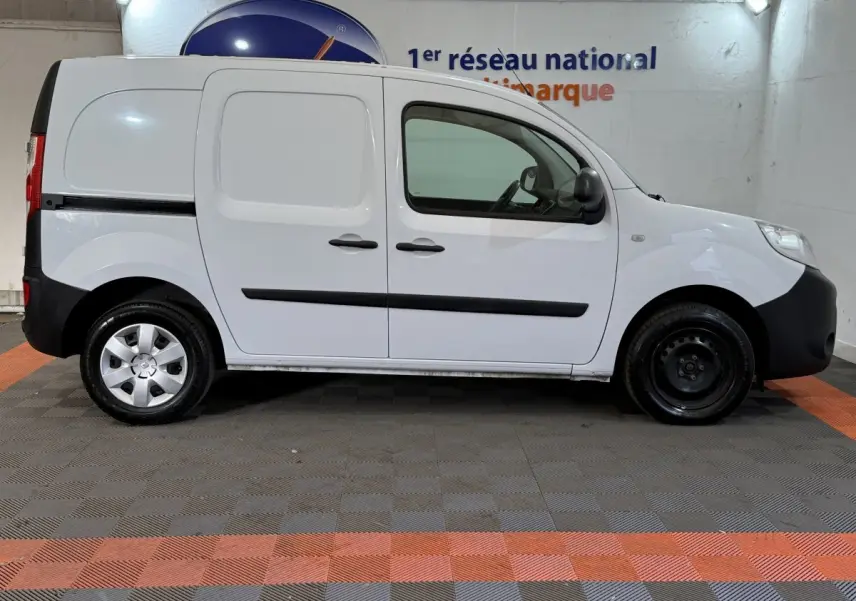 Profil droit d’un Renault Kangoo blanc utilitaire avec portes latérales pleines et jantes acier, en intérieur showroom.