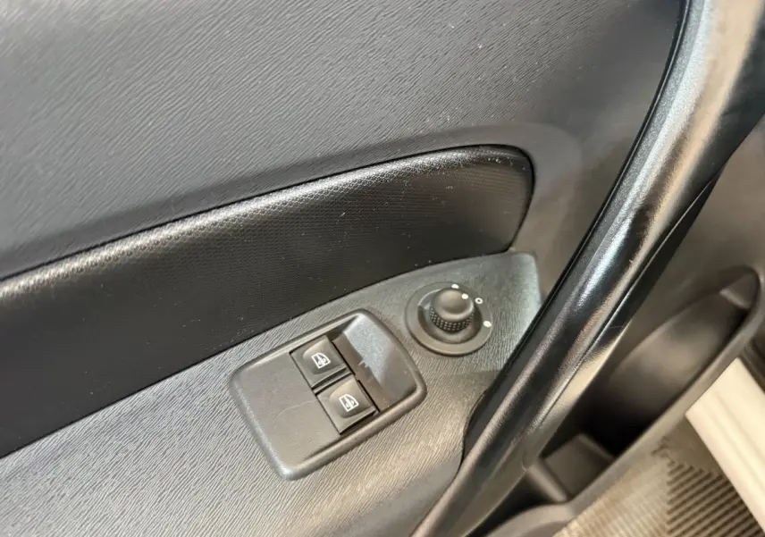 Gros plan sur les commandes de lève-vitres et réglage des rétroviseurs côté conducteur d’une Renault Kangoo blanche.