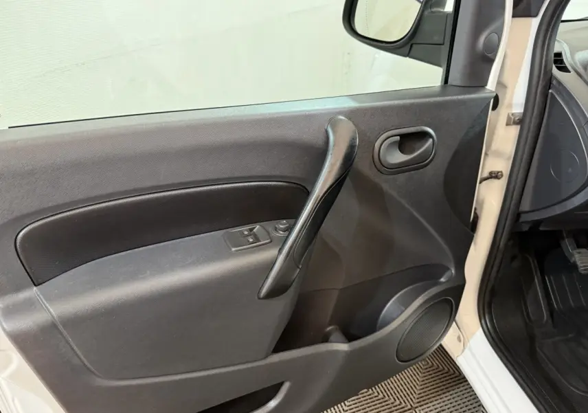 Vue intérieure côté gauche de la porte avant d’un Renault Kangoo blanc avec poignée noire et commandes de vitres électriques.