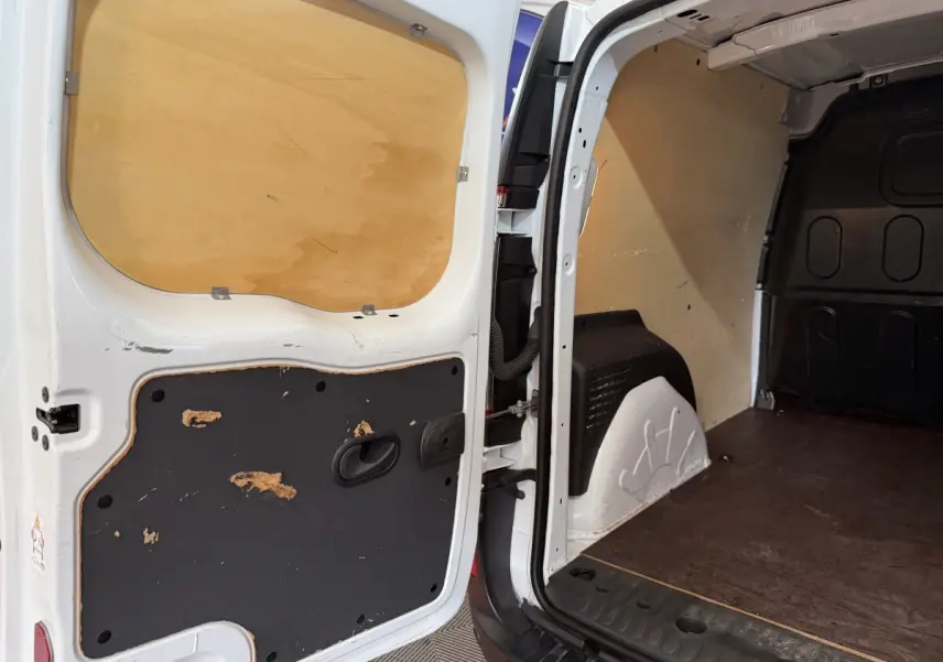 Vue intérieure arrière du Renault Kangoo blanc 2021 avec portes ouvertes montrant l’espace de chargement vide et la cloison pleine.