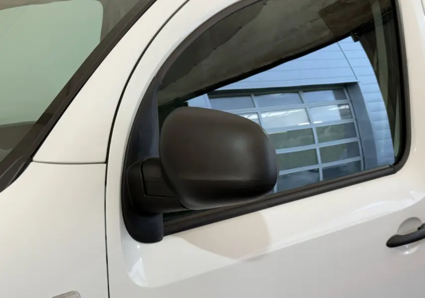Gros plan sur le rétroviseur noir côté conducteur du Renault Kangoo blanc, avec la porte avant visible en arrière-plan.