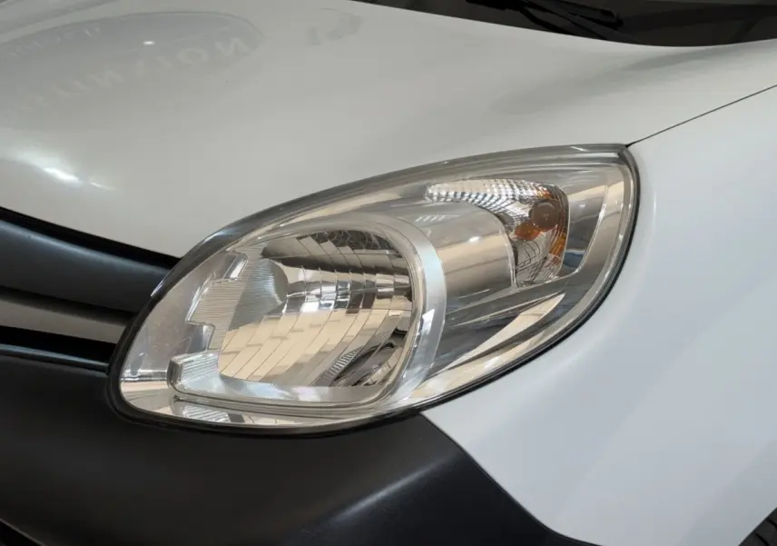 Gros plan sur le phare avant droit du Renault Kangoo blanc, soulignant le contour clair et la calandre noire adjacente.