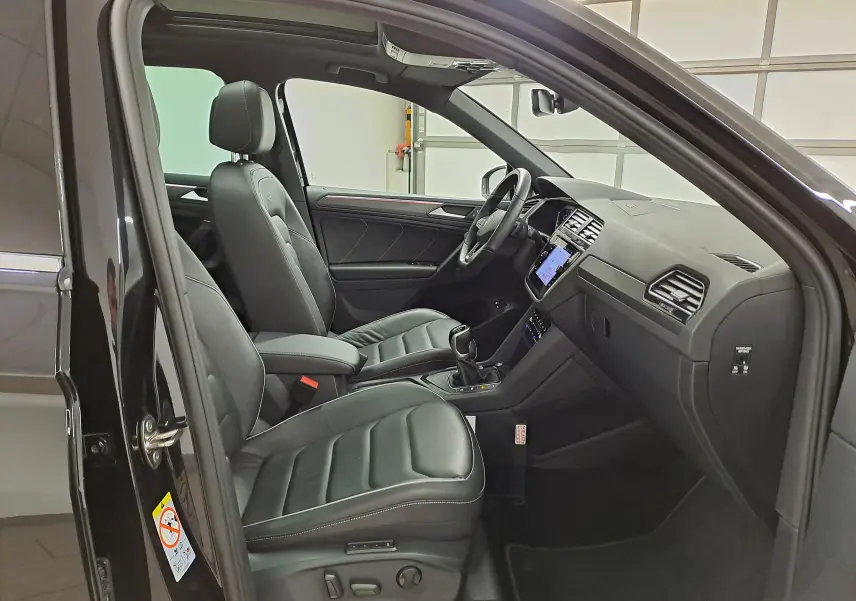 Vue intérieure côté conducteur du Volkswagen Tiguan 1.4 eHybrid 2023 avec sièges cuir noirs et tableau de bord moderne.