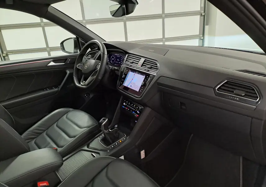 Vue intérieure côté conducteur du Volkswagen Tiguan 2023, tableau de bord noir avec écran tactile et volant multifonction.