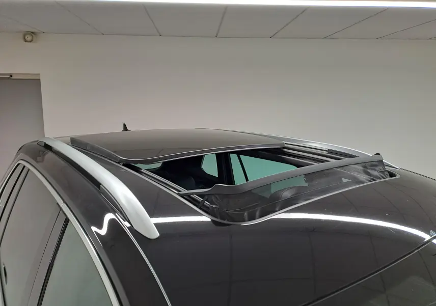 Vue en plongée du toit noir intense nacré d'un Volkswagen Tiguan 2023 avec toit ouvrant panoramique partiellement ouvert et barres de toit argentées.