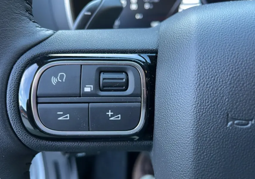Gros plan sur les commandes vocales et de volume à gauche du volant cuir du Citroën C5 Aircross Hybrid blanc 2025.