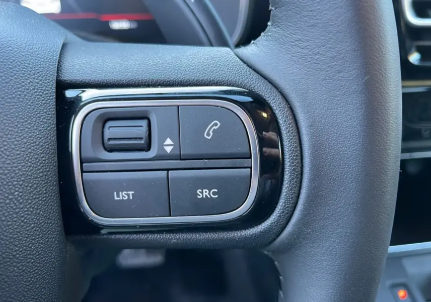 Gros plan sur les commandes gauche du volant cuir du Citroën C5 Aircross blanc okénite, version hybride 2025.