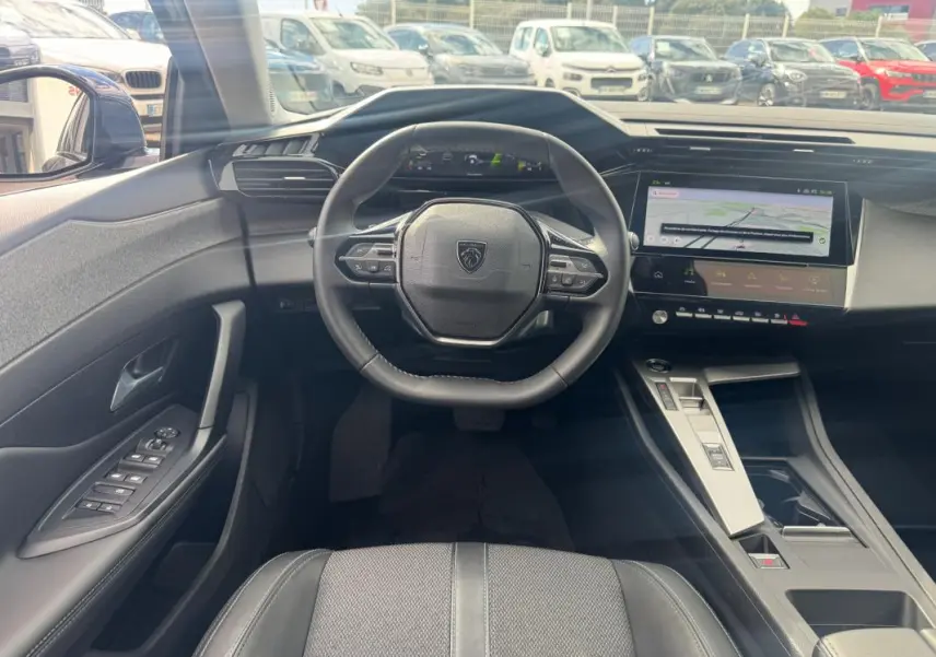 Vue intérieure avant du Peugeot 308 Hybrid gris, montrant le volant compact, le cockpit numérique et l'écran tactile central.