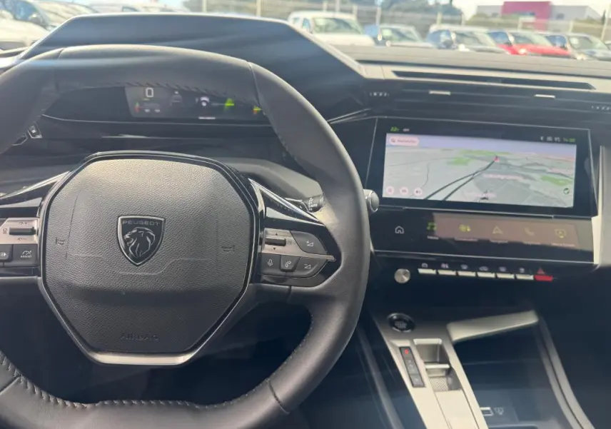 Vue intérieure centrée sur le volant Peugeot et le cockpit numérique avec écran tactile de navigation.