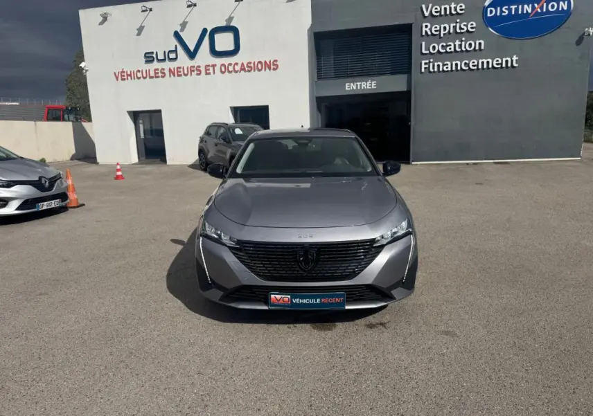 Vue frontale d'une Peugeot 308 Hybrid 145 gris métallisé, avec calandre noire et phares LED fins.